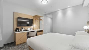 Une chambre d’hôtel moderne dotée d’un grand lit, d’un bureau avec un téléviseur à écran plat, d’une machine à café et d’une armoire.