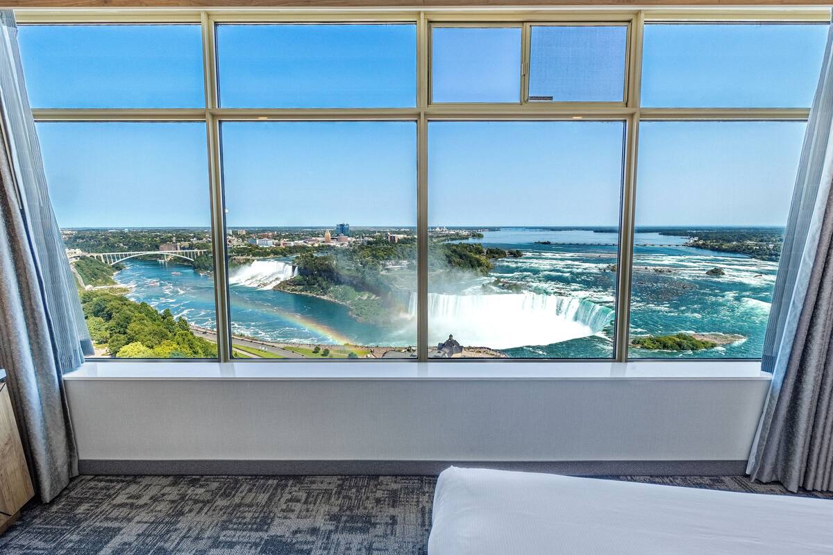 A hotel room with a large window offering a view of a waterfall and a bridge.