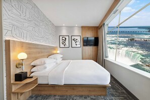 Ein Hotelzimmer mit einem großen Bett, einem Nachttisch mit Lampe, zwei gerahmten Bildern, einem Fernseher und Blick auf einen Wasserfall.