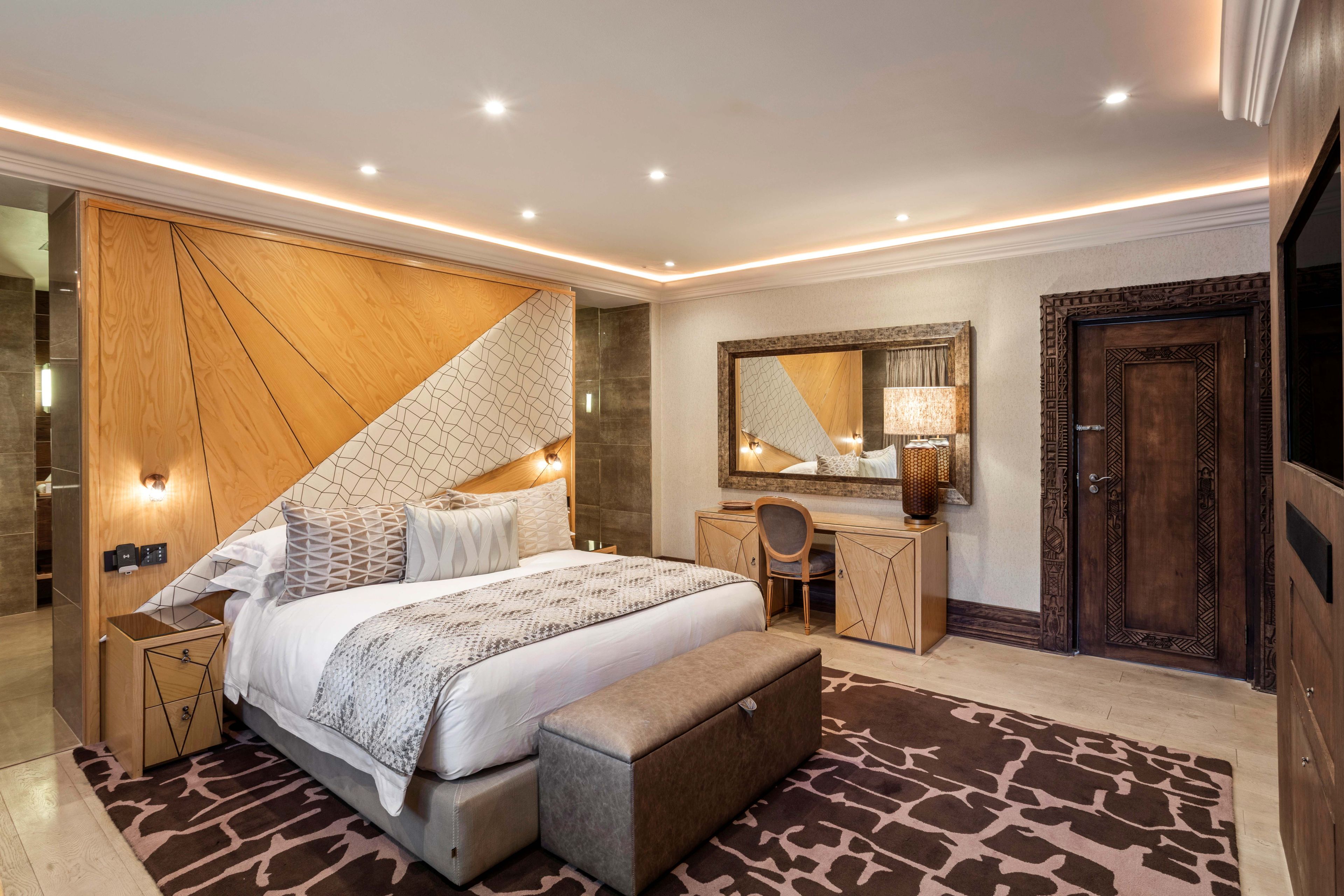 A modern bedroom with a large bed, a desk, a chair, a mirror, and a wardrobe.