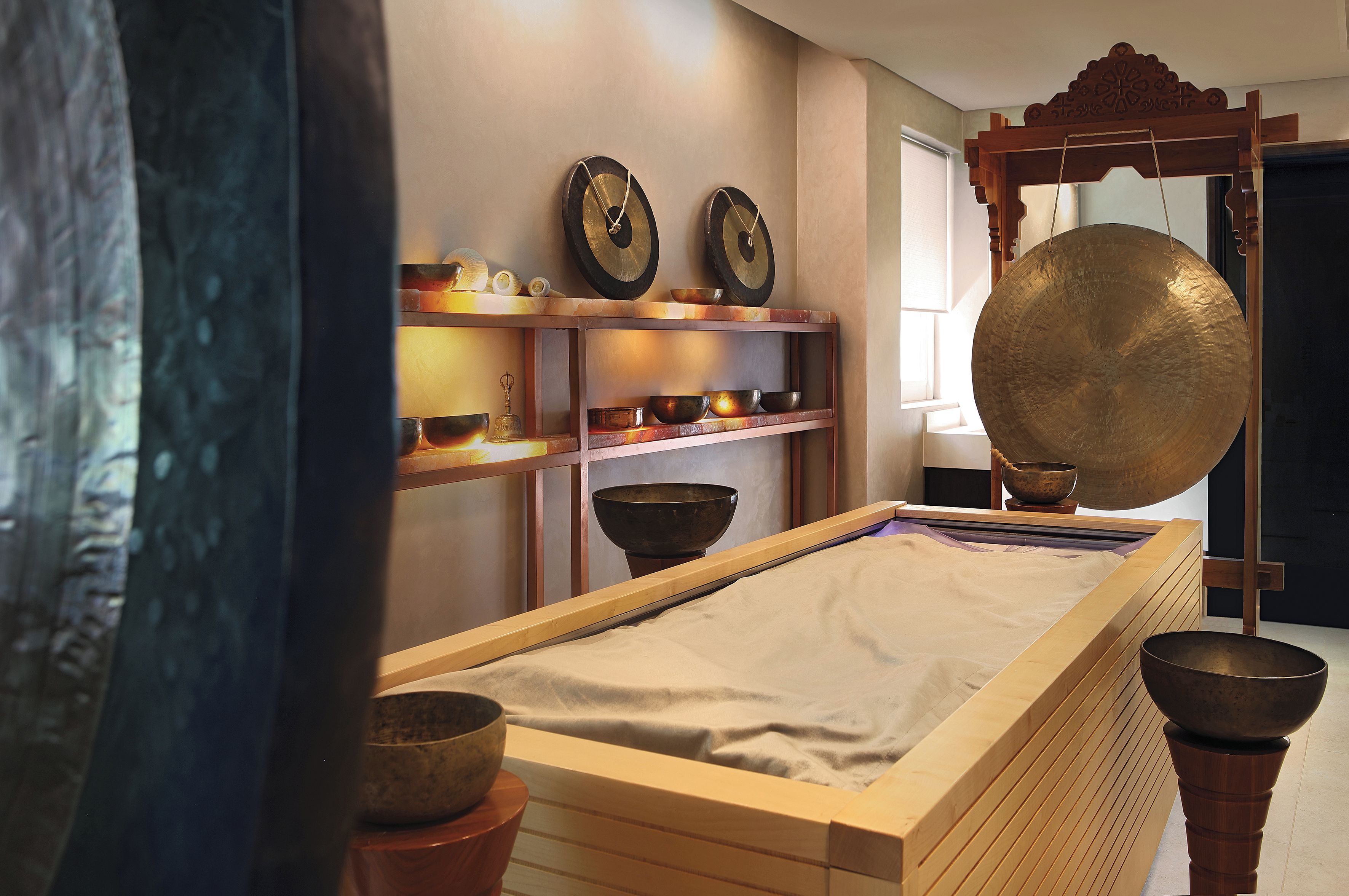 A room with a long wooden table, shelves with bowls, and a large gong.