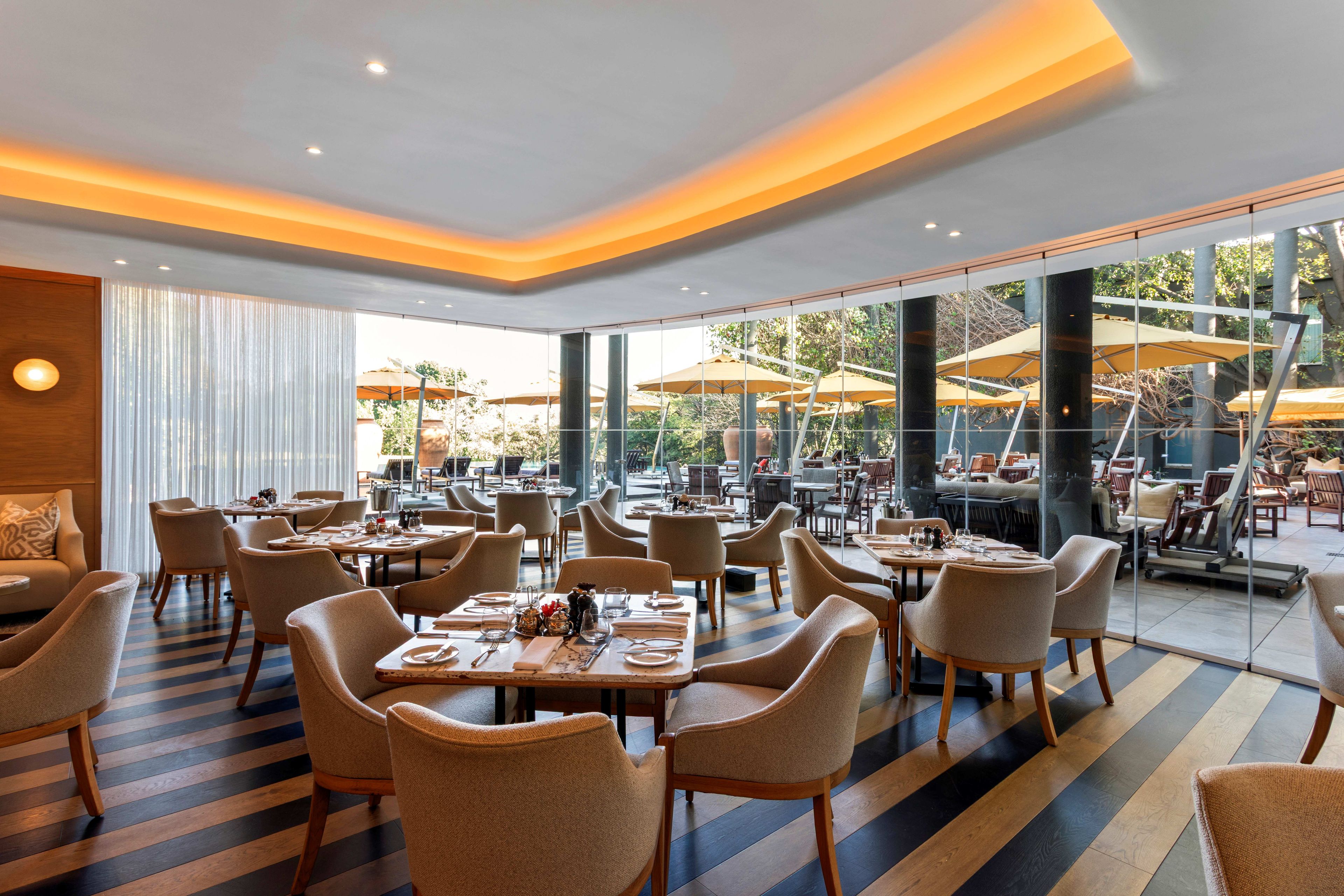 A spacious indoor dining area with multiple tables and chairs, large windows, and outdoor umbrellas.