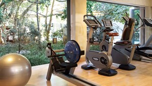 A gym with cardio machines and a large exercise ball, large windows with a view of trees and buildings.