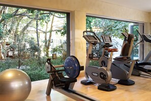 Ein Fitnessraum mit Cardiogeräten und einem großen Trainingsball, große Fenster mit Blick auf Bäume und Gebäude.