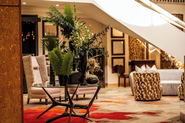 Ein modernes Wohnzimmer mit Glastisch, gemustertem Sofa und dekorativen Pflanzen.