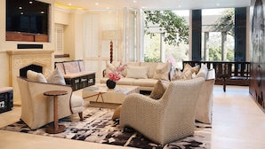 A spacious living room with a fireplace, comfortable seating, and a large window offering a view of the outdoors. - Saxon Hotel, Villas and Spa (Sandton)