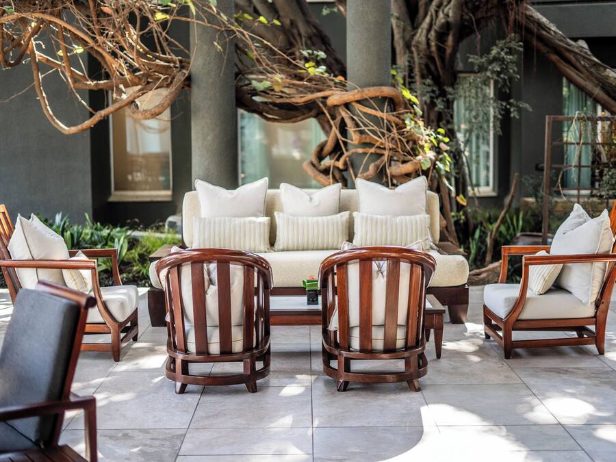 Een zithoek met een bank en stoelen, omringd door een tuin met grote bomen en planten.