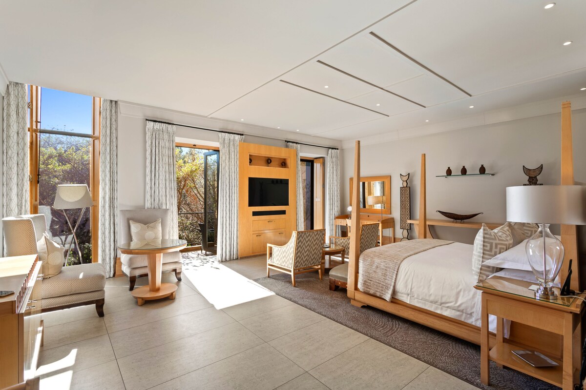 Ein modernes Hotelzimmer mit einem großen Bett, einem Fernseher, einem Schreibtisch und einer Sitzecke mit Stühlen.
