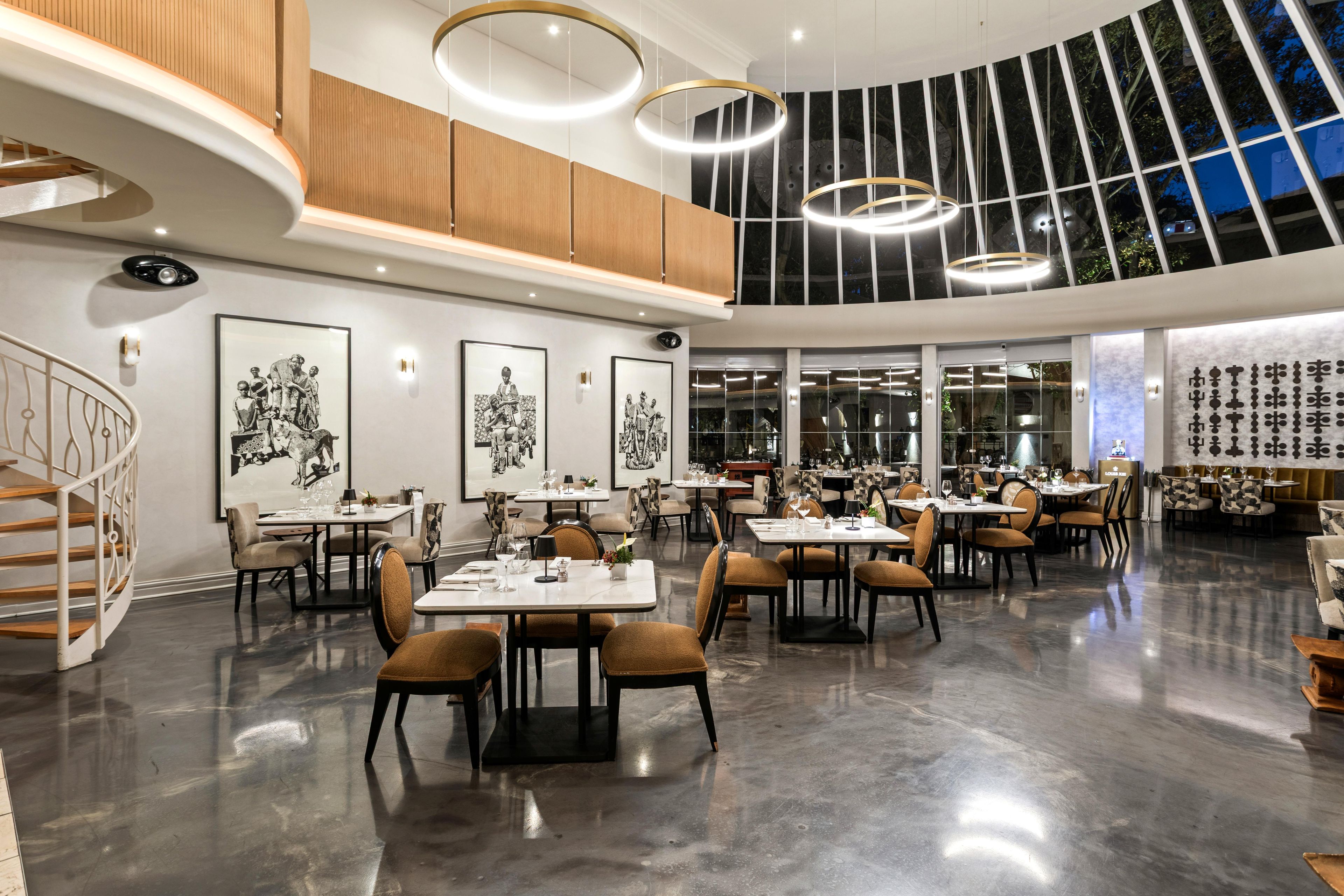 Un restaurant moderne avec un plafond haut, des luminaires circulaires et une vue sur le ciel nocturne grâce à de grandes fenêtres.