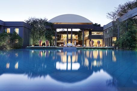 A modern hotel with a large pool, outdoor seating, and a covered area with large vases.