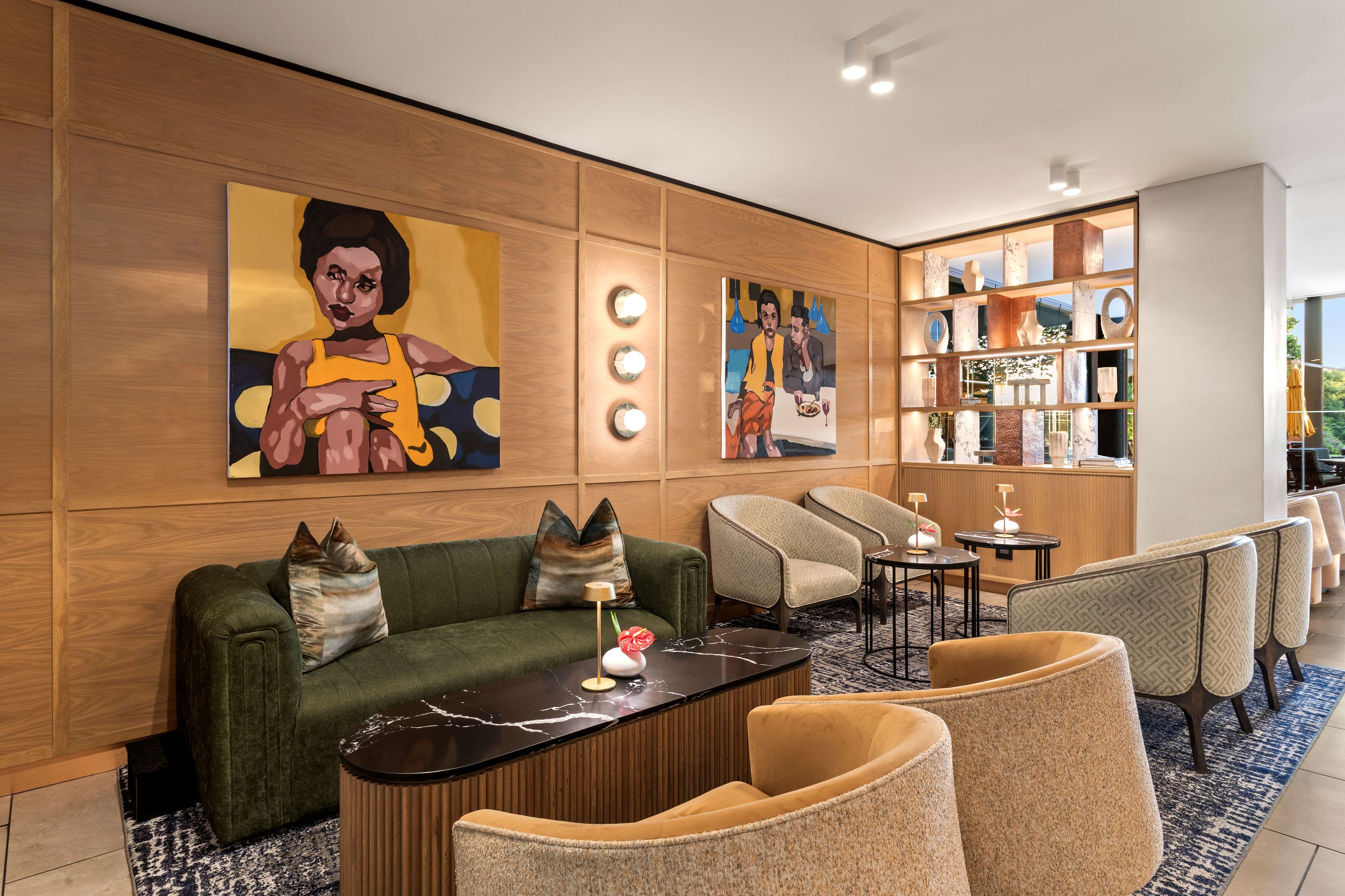 A modern lobby with a green sofa, armchairs, a marble coffee table, and a large painting on the wall.