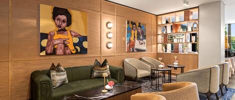 A modern lobby with a green sofa, armchairs, a marble coffee table, and a large painting on the wall.