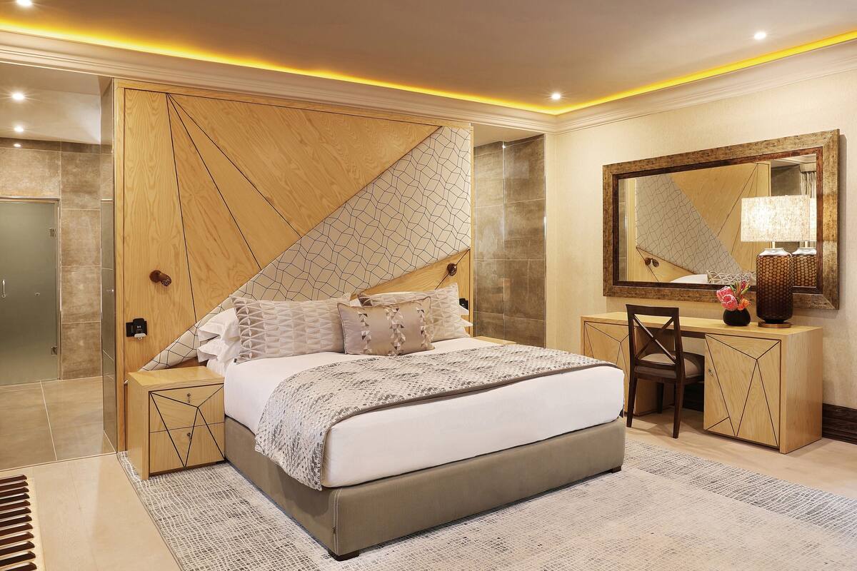 Un dormitorio moderno con una cama grande, cabecera de madera, mesitas de noche, un escritorio y un espejo.