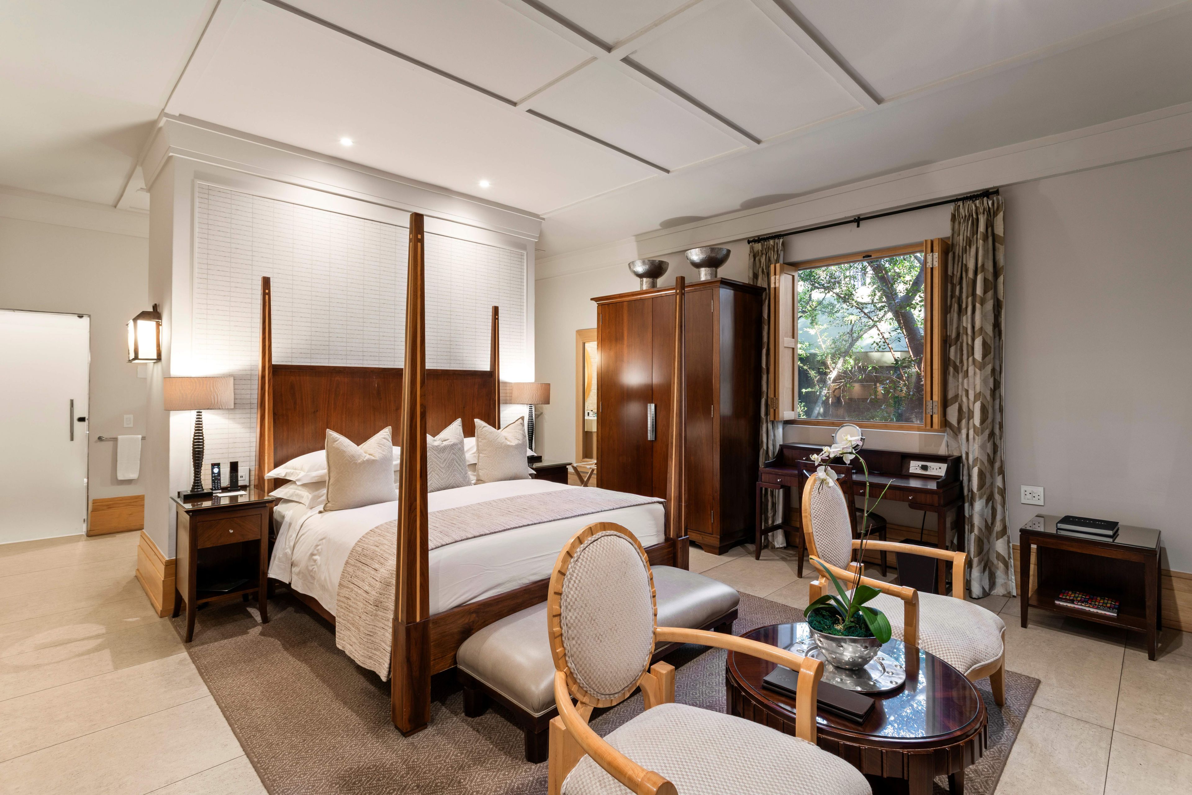 Una habitación de hotel con una cama grande, un escritorio, una silla, una mesita y una ventana con cortinas.