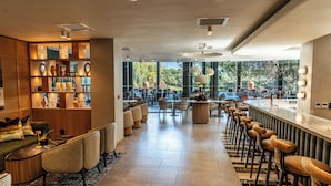 A modern bar area with a long counter, bar stools, and a seating area with sofas and chairs. - Saxon Hotel, Villas and Spa (Sandton)