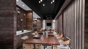 A modern dining area with a long wooden table, cushioned chairs, and a central chandelier. - Marriott North Austin Round Rock (Round Rock)