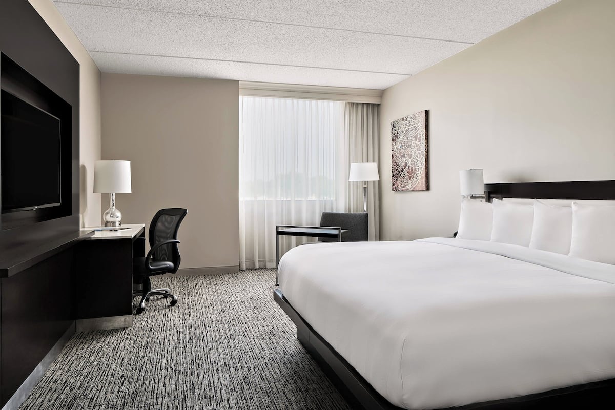 A hotel room with a large bed, a desk with a chair, a flat-screen TV, and a window with curtains.
