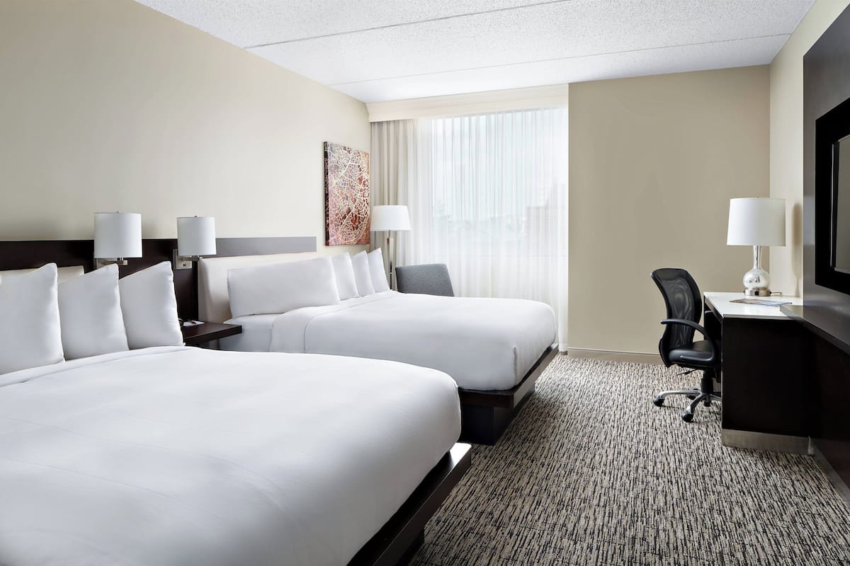 A hotel room with two beds, a desk, a chair, a TV, and a window with curtains.