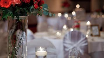 A table setting with a tall glass vase containing red flowers and greenery, a lit candle, and clear glassware.