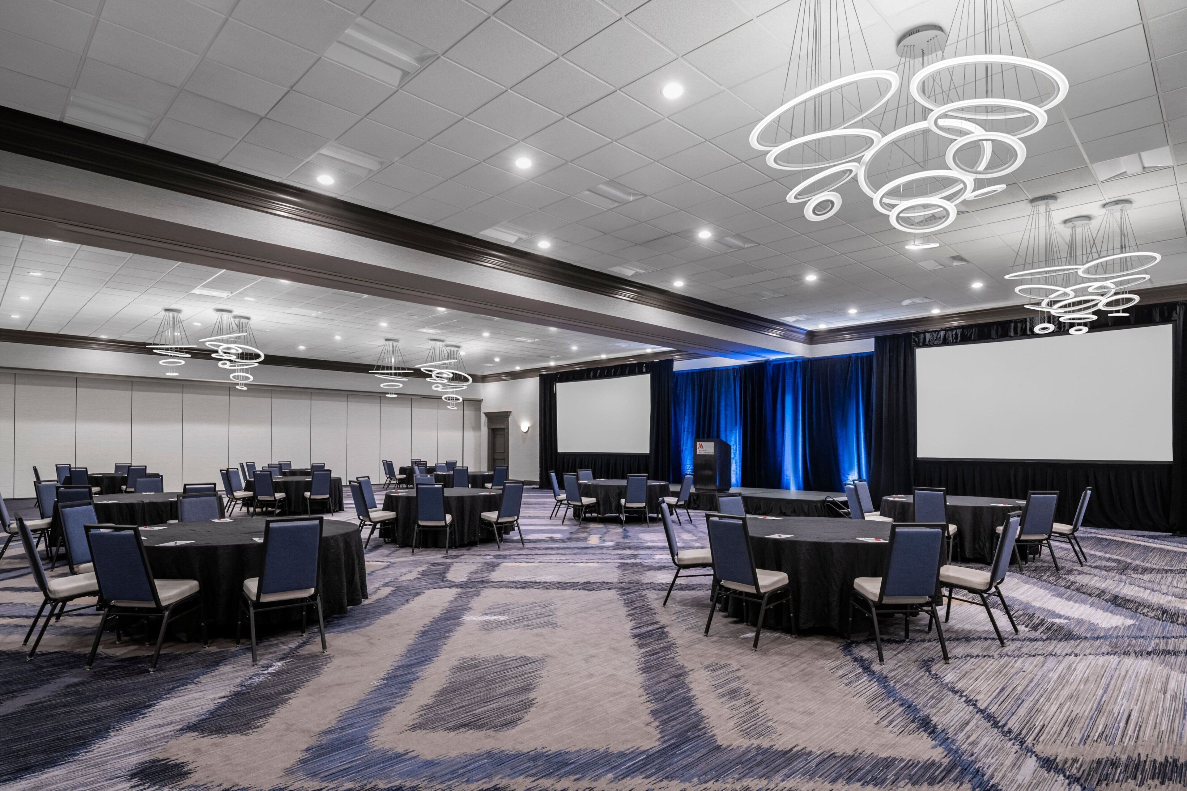 A conference room with round tables, chairs, and a large screen.