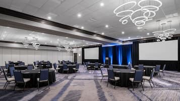 A conference room with round tables, chairs, and a large screen.