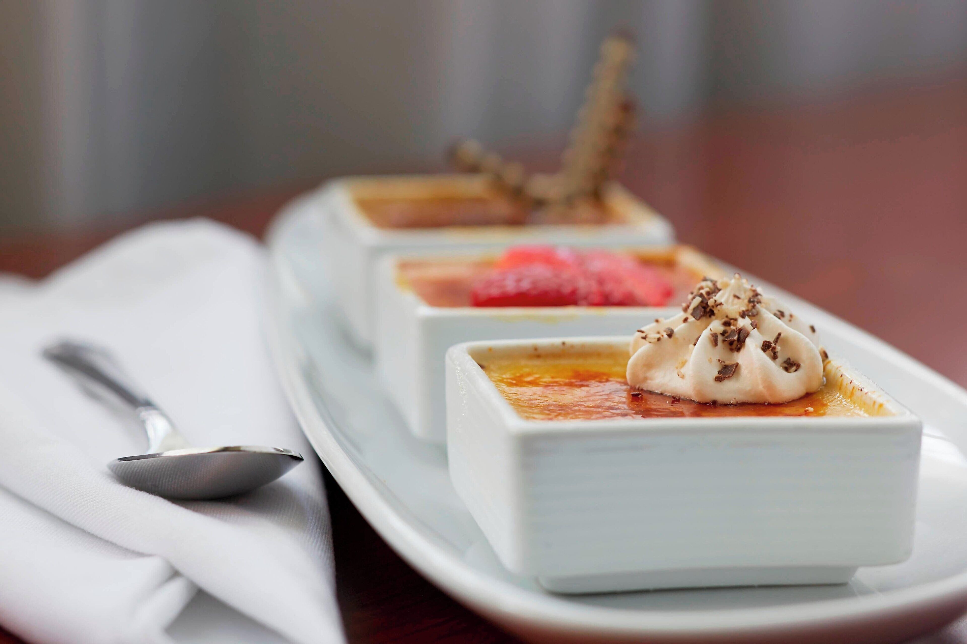 Tres platos blancos cuadrados con postres sobre una bandeja blanca.