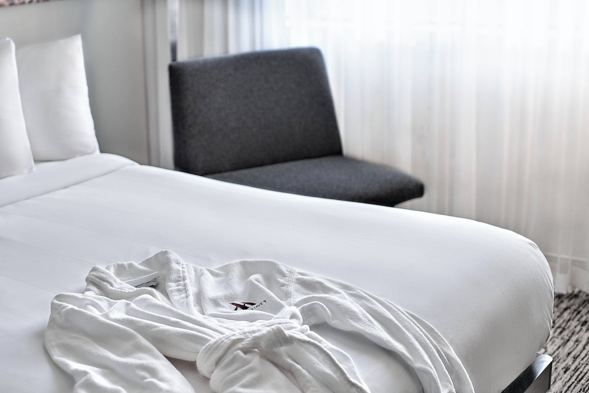 A neatly made bed with white bedding and a white robe on it.