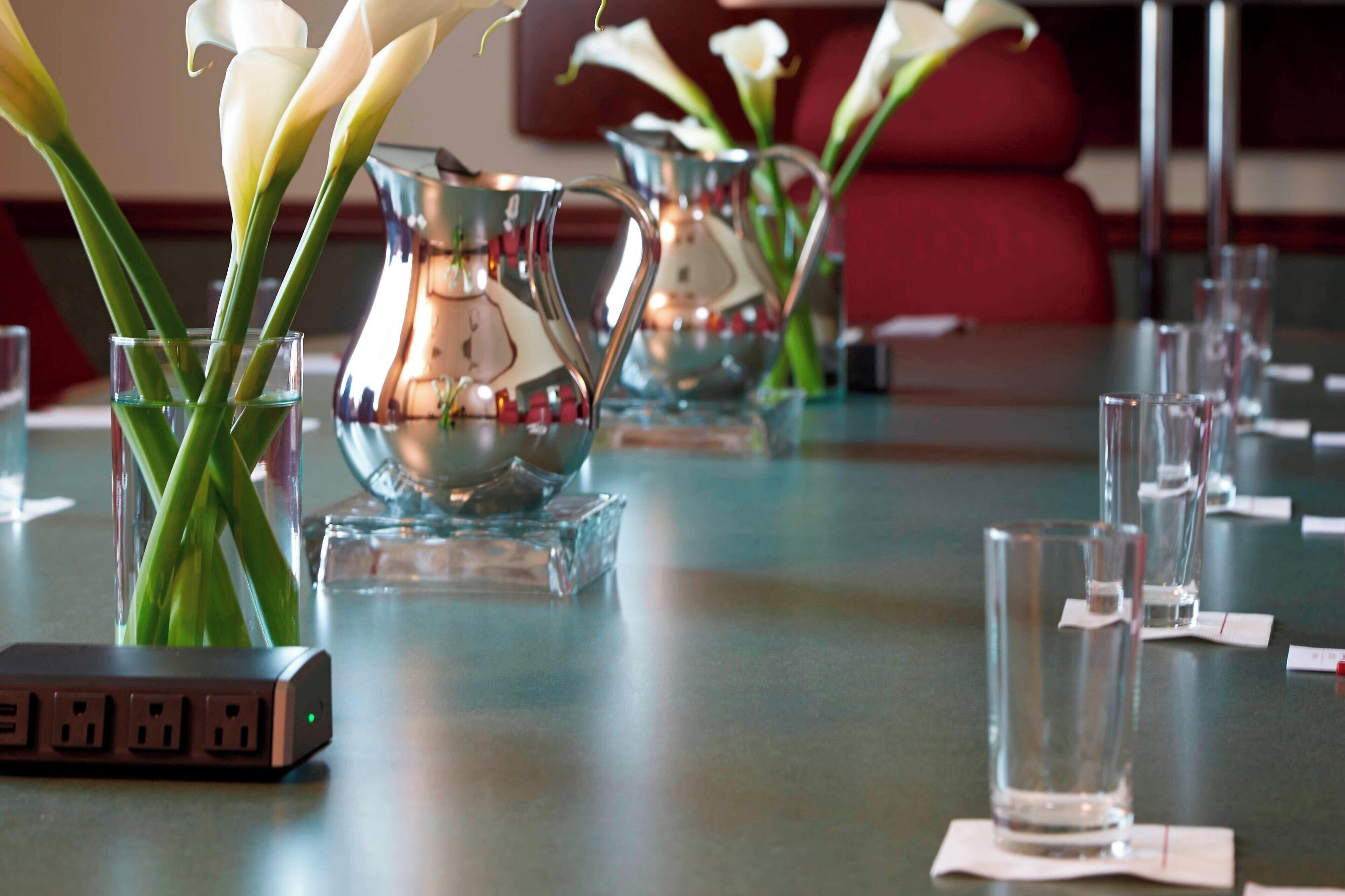 A table set with clear glassware, a silver pitcher, and a vase with white flowers.