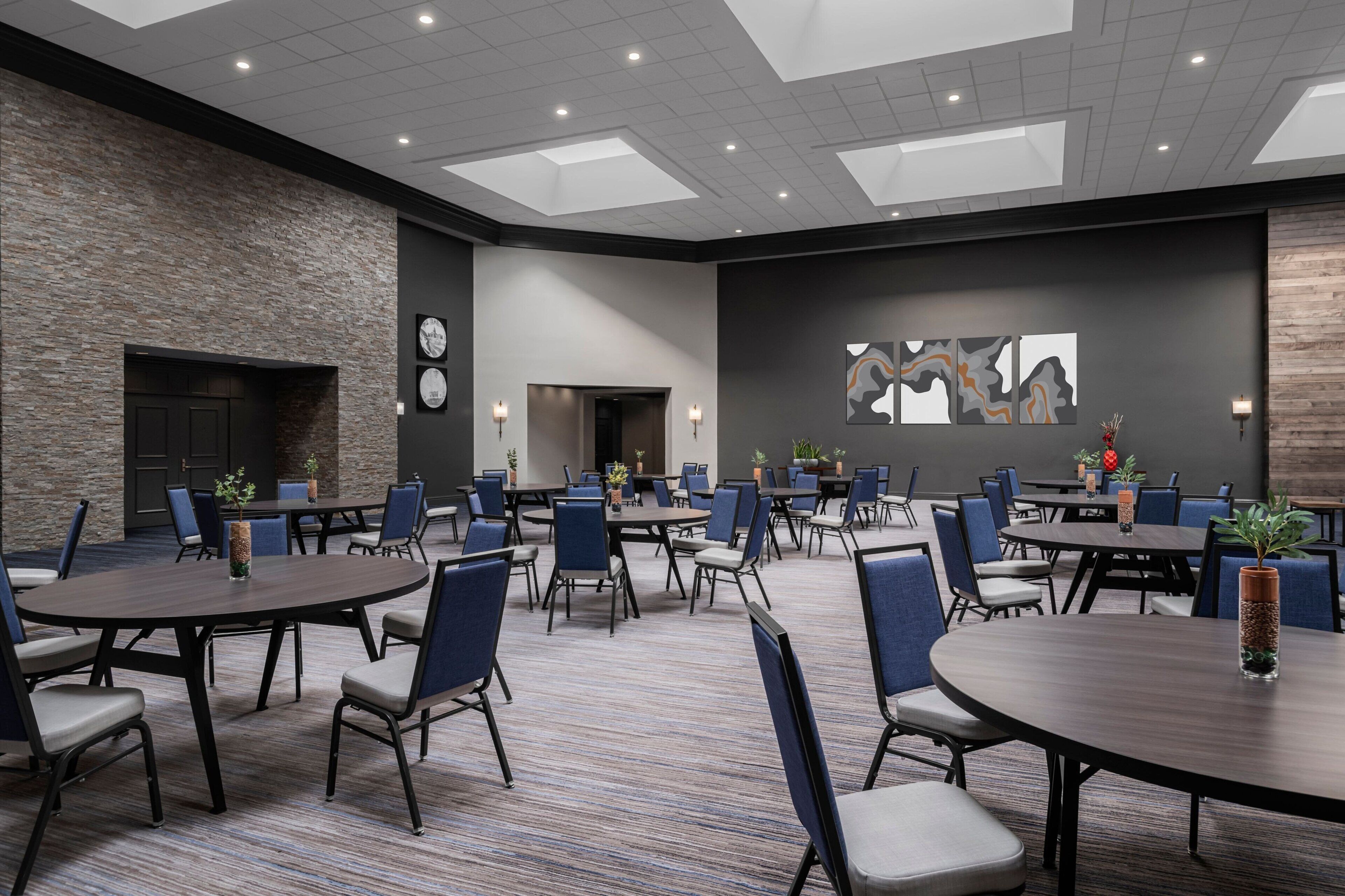 A conference room with multiple tables and chairs, a stone wall, a fireplace, and artwork on the wall.