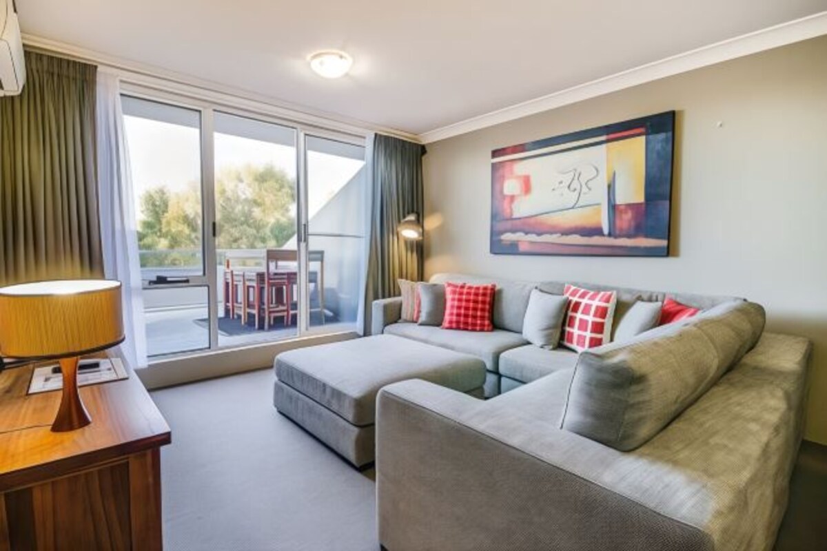 A modern living room with a grey sofa set, a wooden side table, and a large window with curtains.