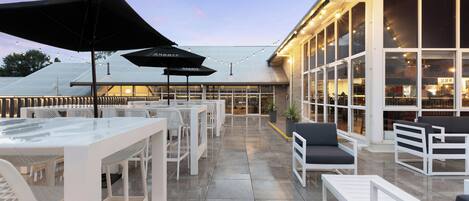 An outdoor patio with white furniture, umbrellas, and string lights.