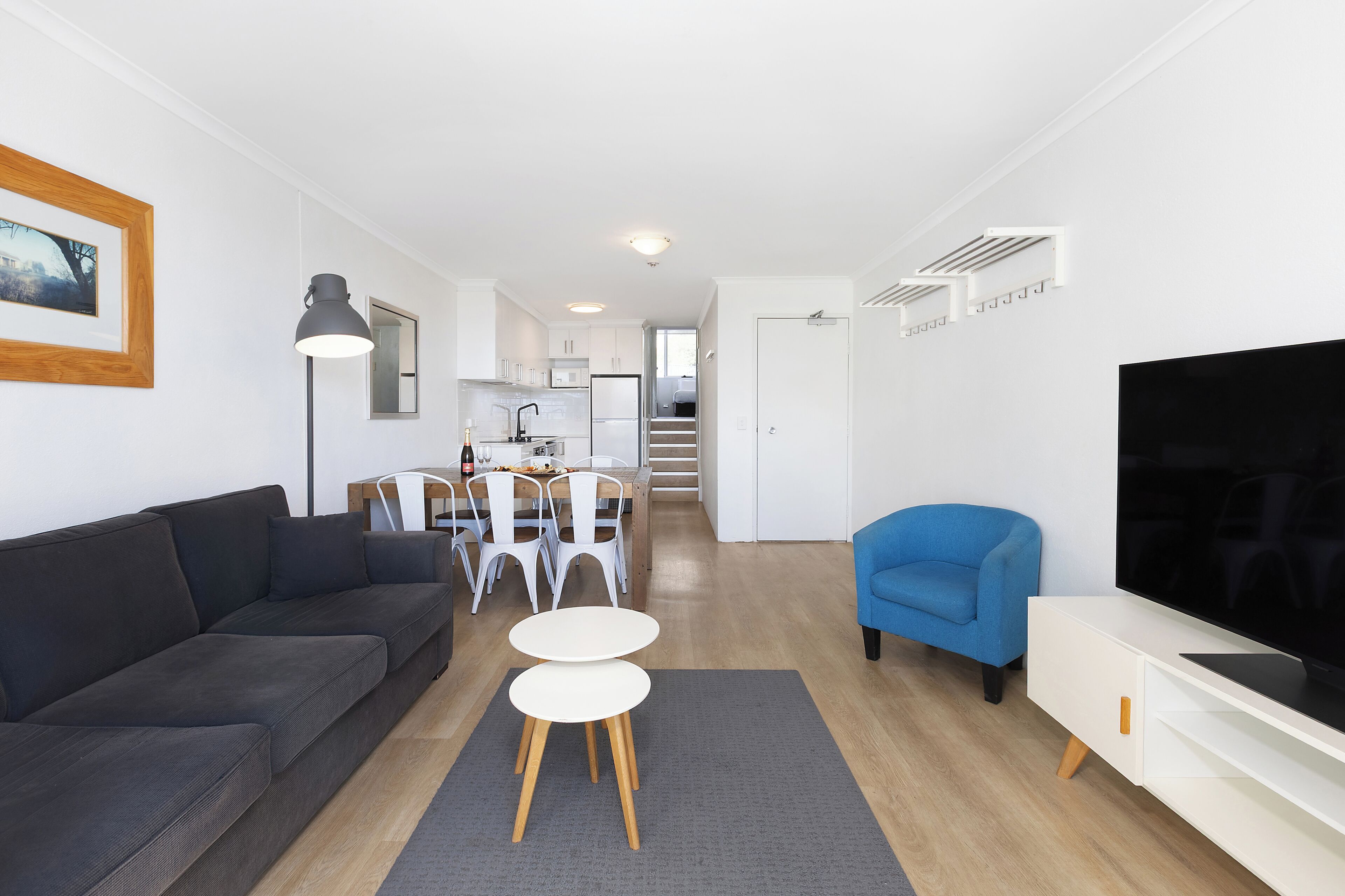 Een moderne woonkamer met een bank, een televisie, een eethoek met stoelen en een tafel, en een trap naar een verdieping erboven.