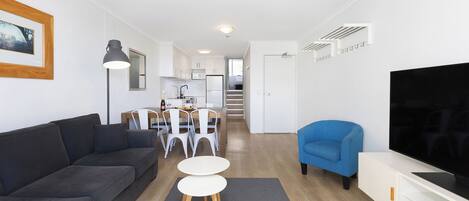 Ein modernes Wohnzimmer mit einer Couch, einem Fernseher, einem Essbereich mit Stühlen und einem Tisch sowie einer Treppe, die zu einer oberen Etage führt.