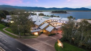 Un hotel grande y moderno con un área exterior amplia, un patio cubierto y vistas a un lago y montañas.