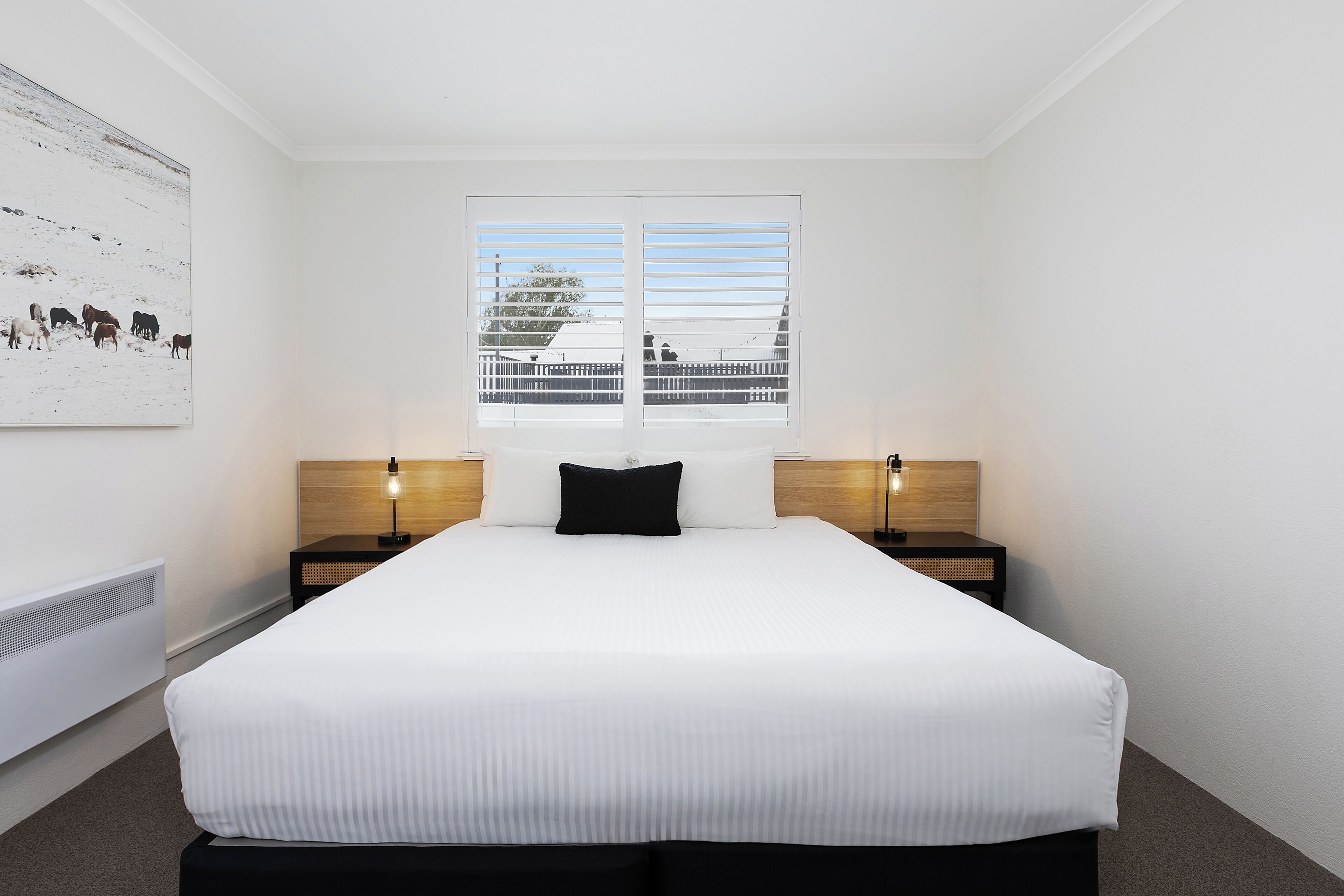 A hotel room with a large bed, two bedside tables, a window with a view, and a wall-mounted artwork.