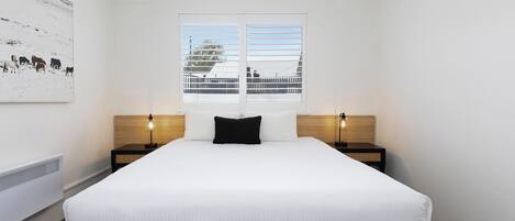 A hotel room with a large bed, two bedside tables, a window with a view, and a wall-mounted artwork.