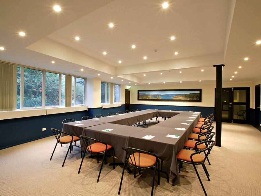Una sala de conferencias con una larga mesa, sillas y ventanas grandes con cortinas.