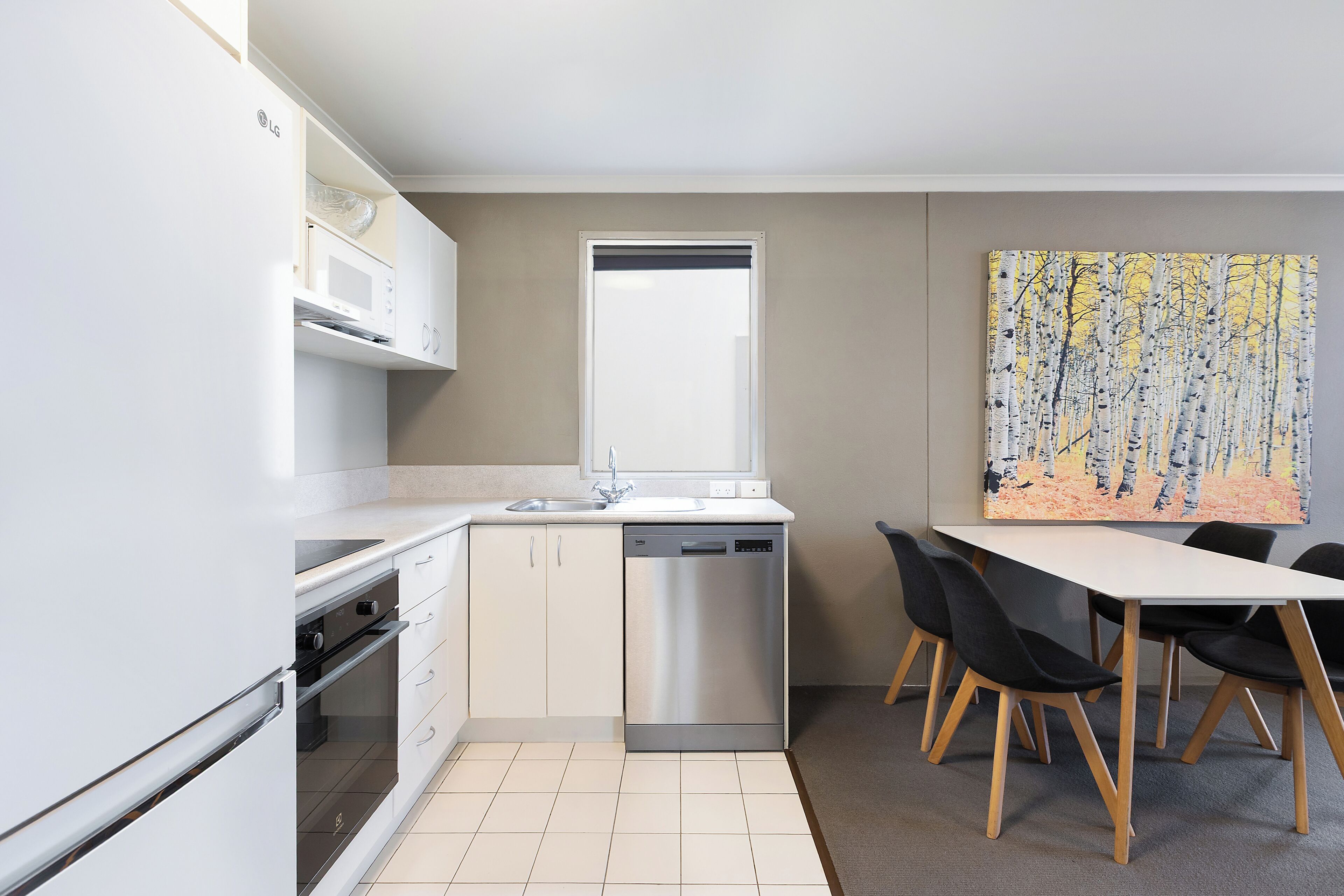 Una cucina moderna con mobili bianchi, una lavastoviglie e un'area pranzo con tavolo e sedie.