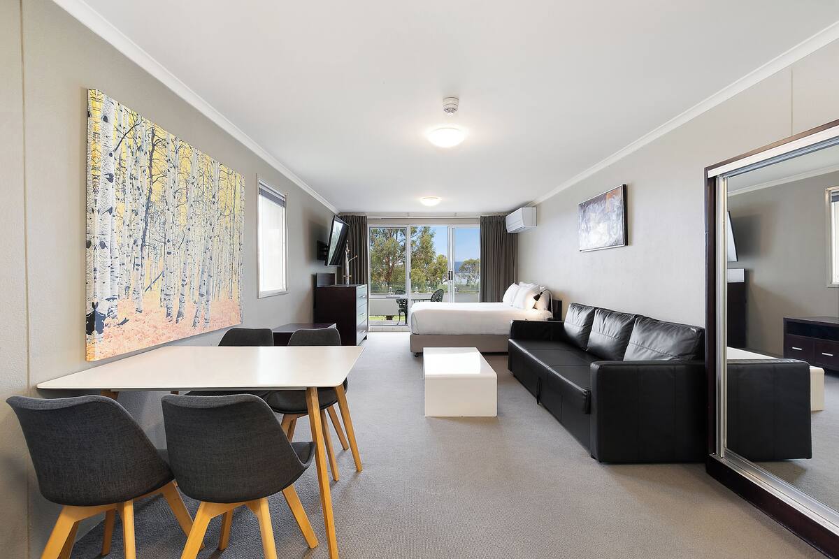 A modern hotel room with a dining area, a sofa, a bed, and a large mirror.