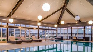 Una piscina interior moderna con paredes de vidrio transparente, sillones de descanso e iluminación en el techo.
