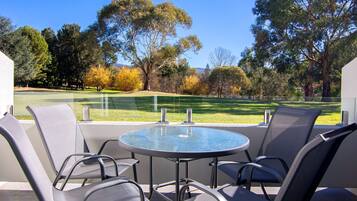 A round glass table with four chairs, a view of a golf course, and a clear sky.