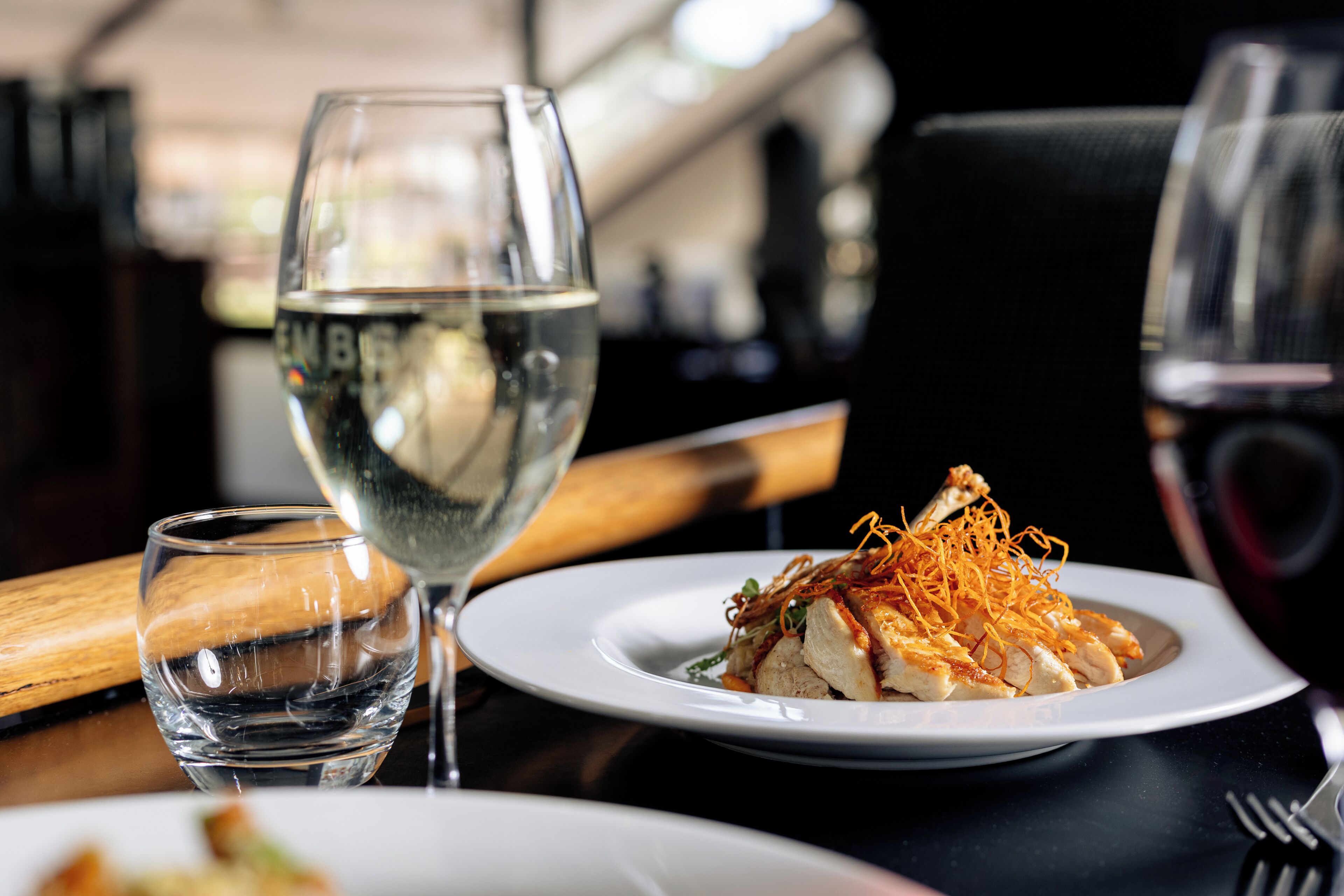 A dining table with a plate of food, a glass of white wine, and a glass of water.