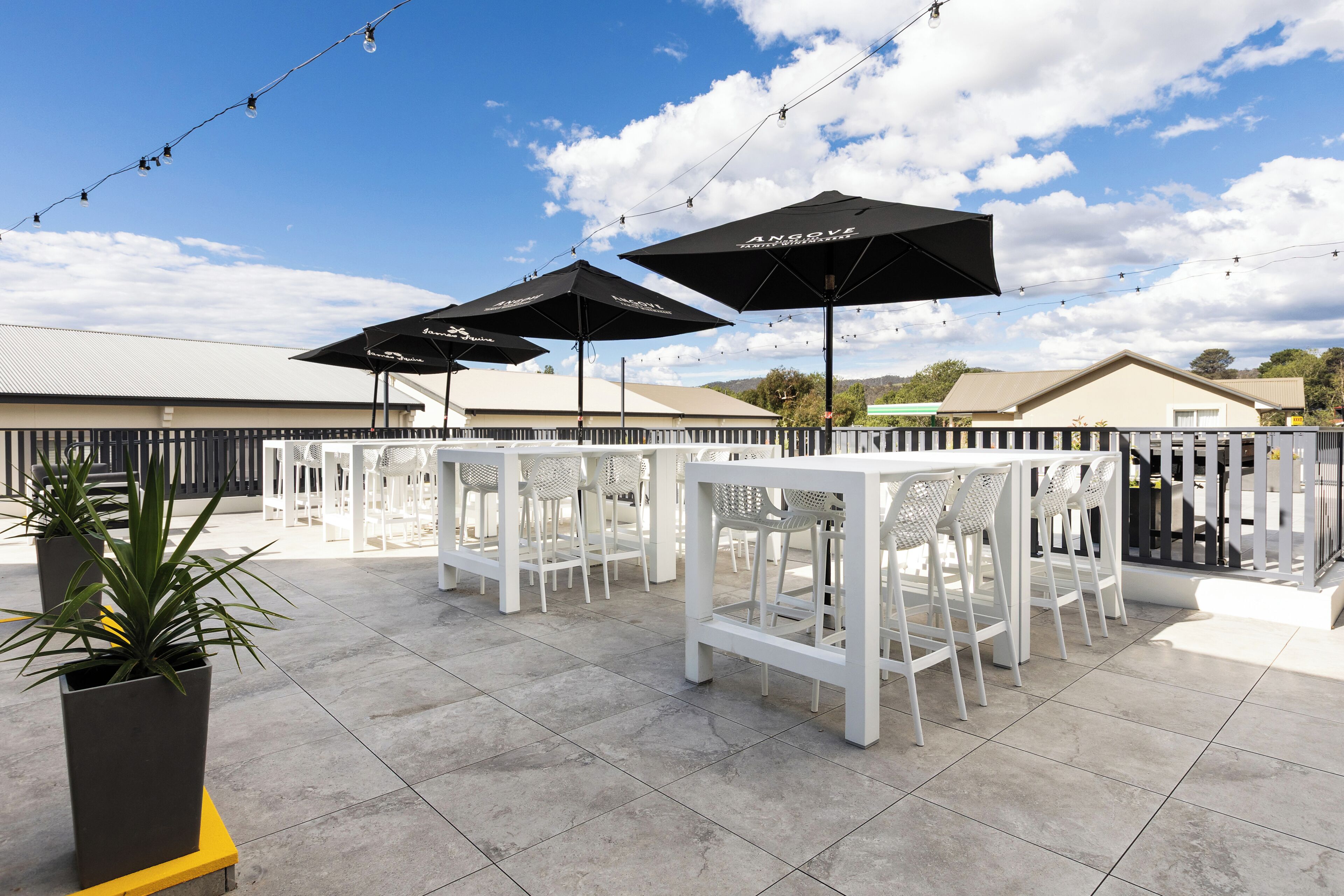 An outdoor patio with white furniture, black umbrellas, and string lights.