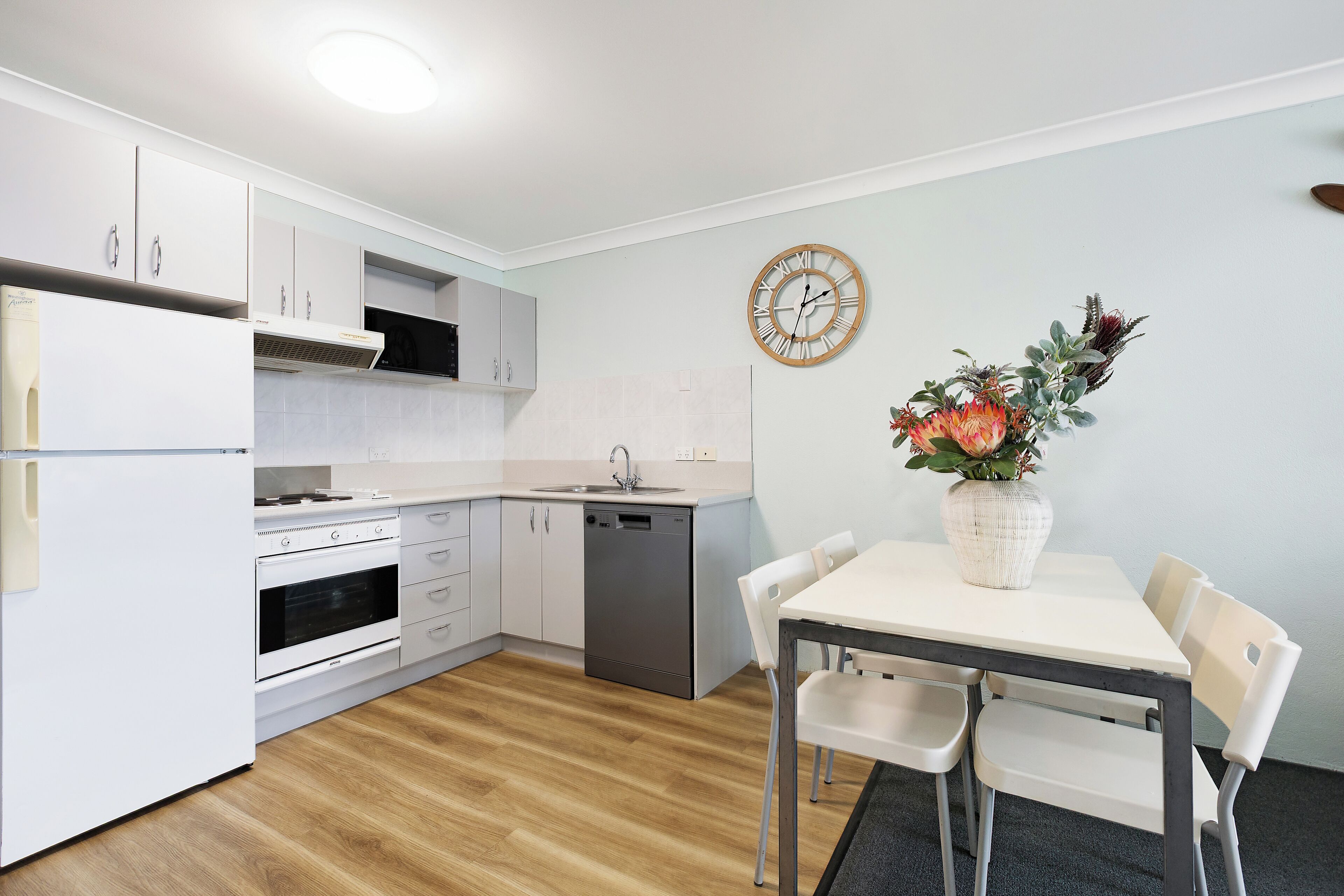 Una cocina moderna con armarios blancos, lavavajillas y un comedor con mesa y sillas.