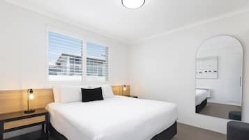 A hotel room with a large bed, two bedside tables, a nightstand, a mirror, and a window with blinds.