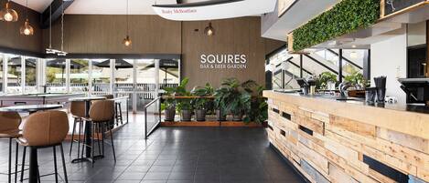 A bar and beer garden with a wooden counter, bar stools, and potted plants.