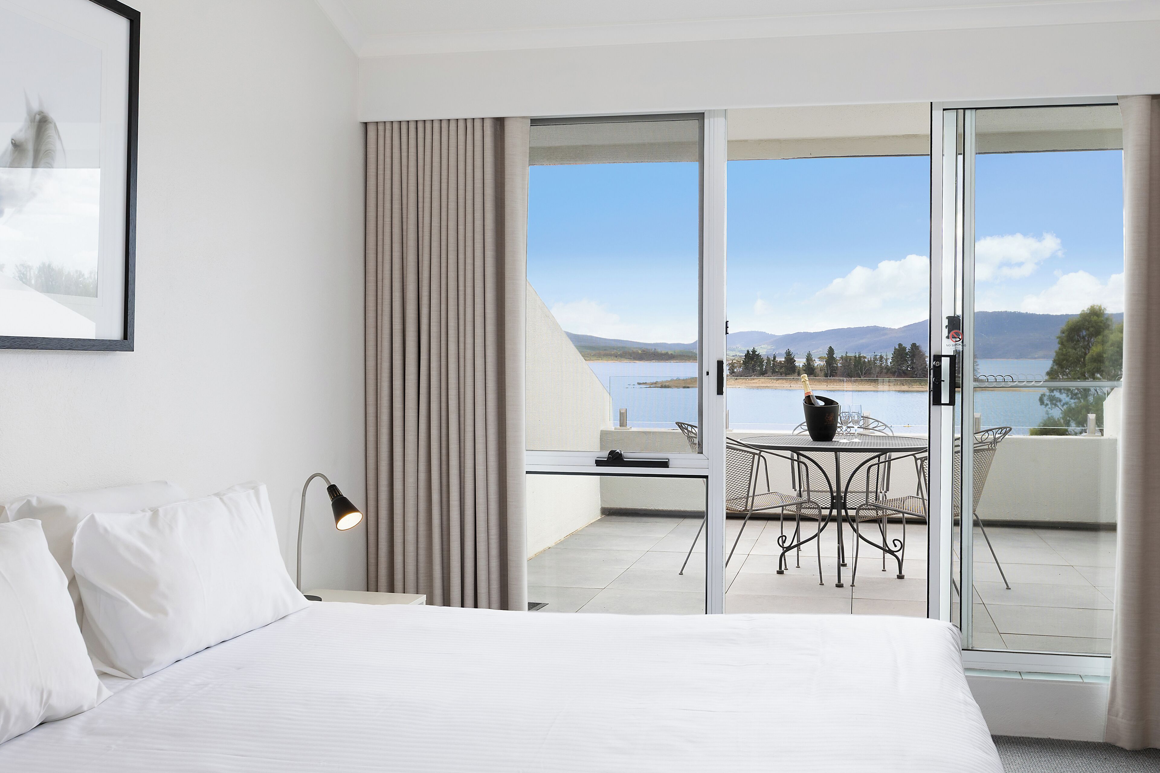 A hotel room with a bed, a desk, and a view of a lake and mountains.