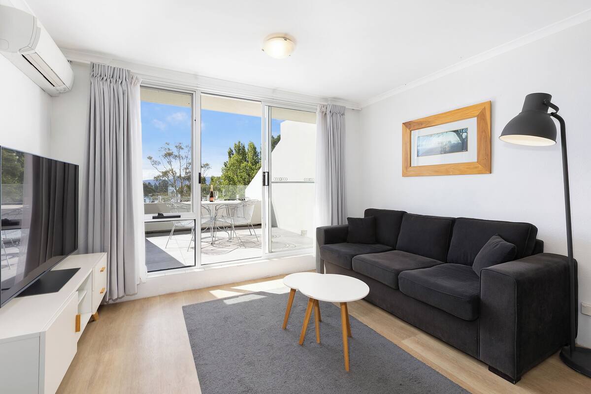 A modern living room with a grey sofa, a small white table, a TV, and a floor lamp.