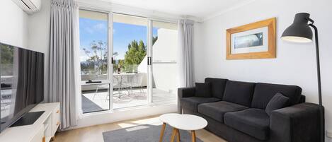 A modern living room with a grey sofa, a small white table, a TV, and a floor lamp.