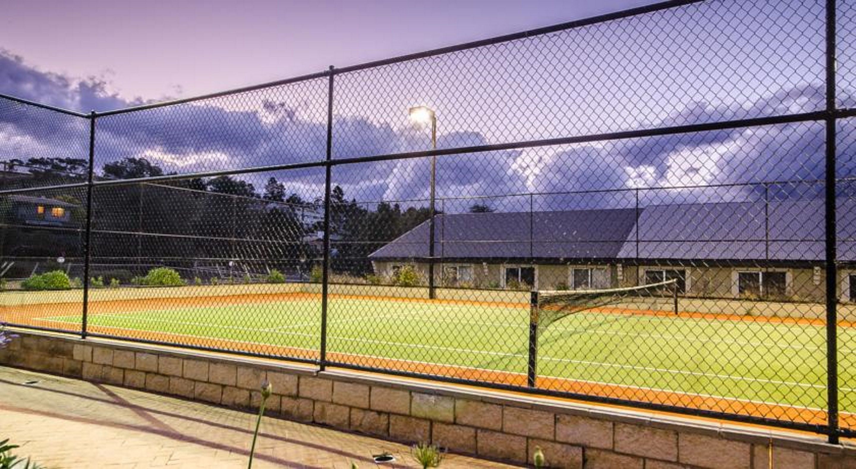 A baseball field enclosed by a chain-link fence with a brick wall at the base, a light post, and a building in the background.